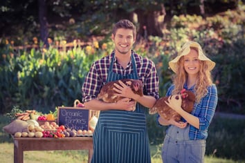 Happy farmers standing at their stall and holding chicken on a sunny day